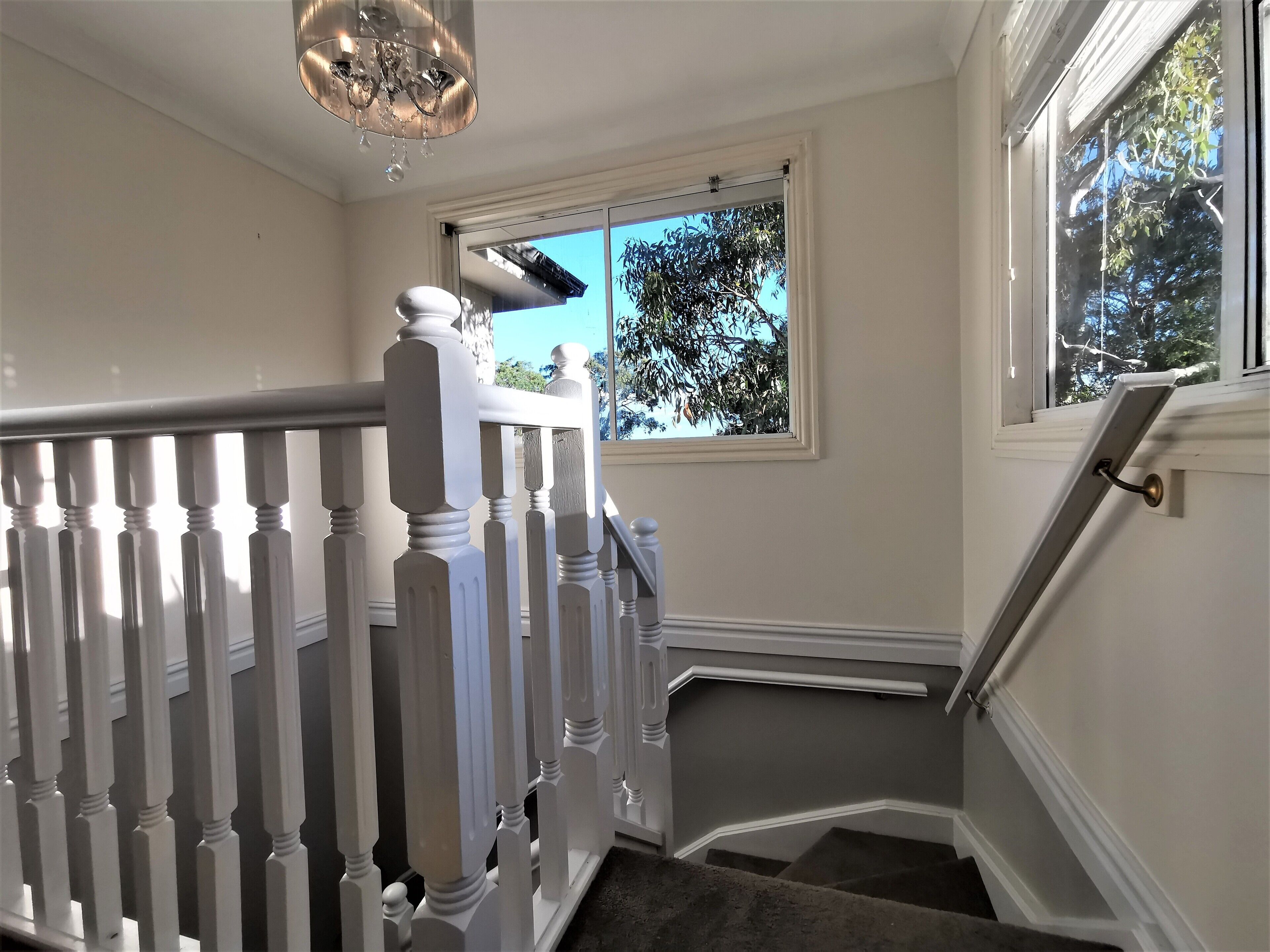 A staircase with white balusters and a handrail, leading to a landing with a window overlooking greenery.