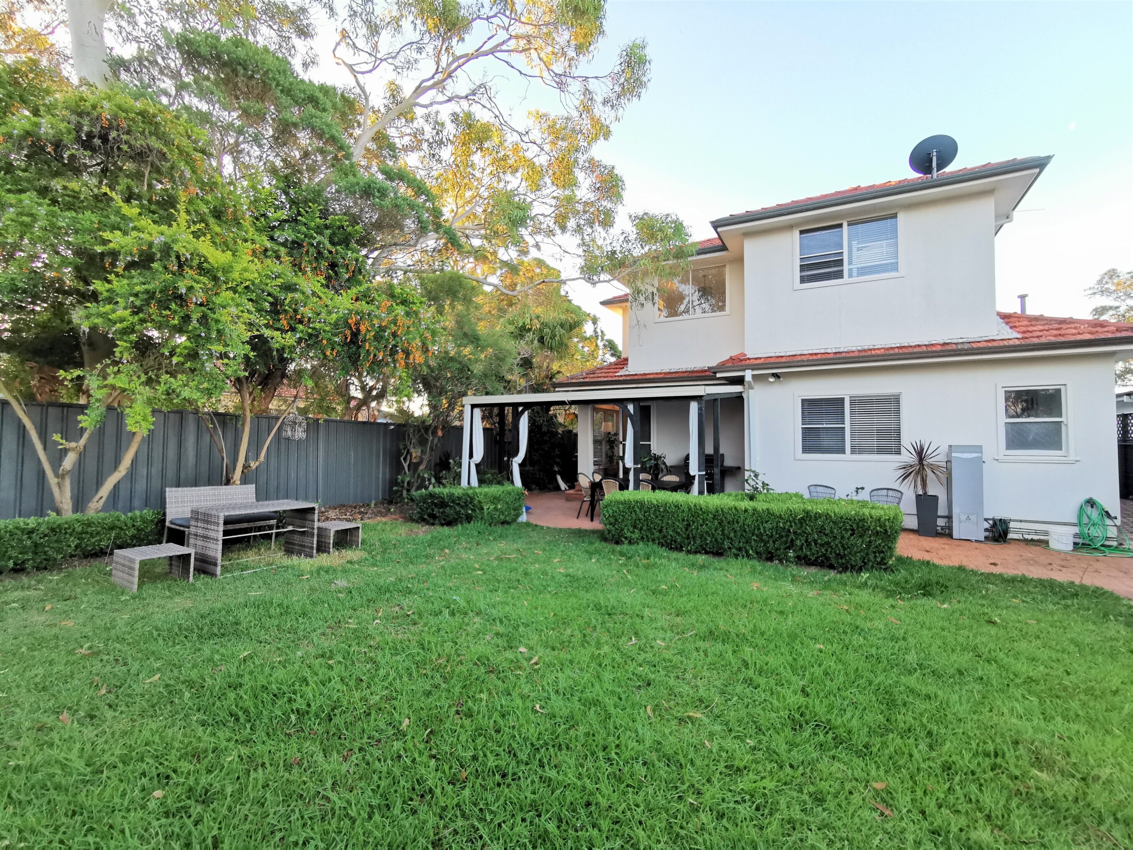 A two-story house with a covered patio, a fenced backyard, and a well-maintained lawn.