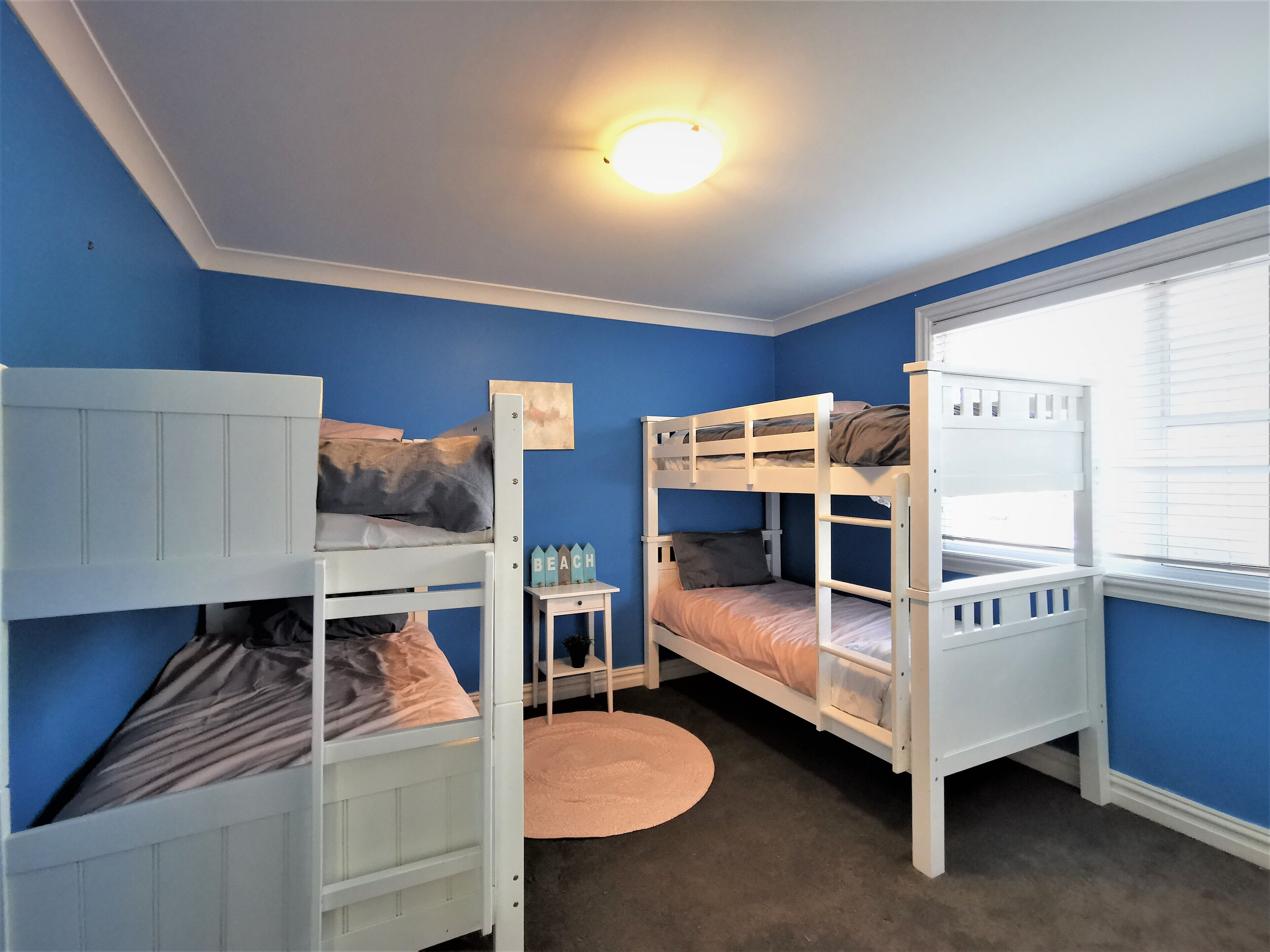 Een kamer met drie stapelbedden, een kleintje tafeltje met een plant en een rond tapijt.