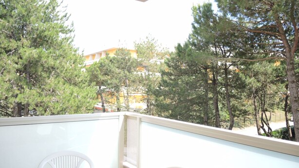 Un balcón con una mesa lista para comer, con vistas a un área boscosa con árboles y un edificio al fondo.