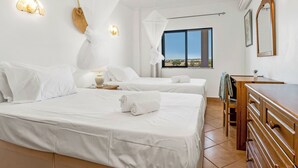 Une chambre d’hôtel avec deux lits, une commode en bois, une fenêtre donnant sur un beau paysage et des lampes fixées au mur.