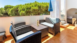 Un balcon agrémenté de meubles en osier, une table avec une bouteille et des verres, et une vue sur des arbres verdoyants.