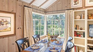A dining area with a wooden table set for four, a window with curtains, and a bookshelf with various items. - 3903 Mabuhay - Walk to Downtown and the Beach (Carmel)