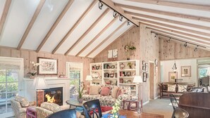 A cozy living room with a fireplace, wooden beams, a sofa, and a dining area with a table set for two. - 3903 Mabuhay - Walk to Downtown and the Beach (Carmel)