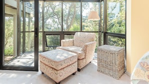 A conservatory with a wicker ottoman, patterned armchair, and a lamp. - 3903 Mabuhay - Walk to Downtown and the Beach (Carmel)
