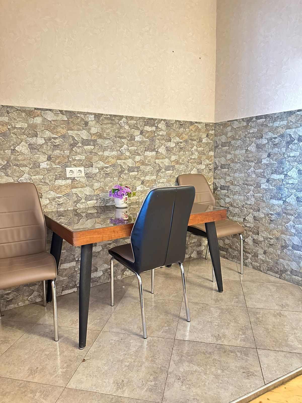 A corner seating area with two chairs and a table, a stone wall, and a tiled floor.