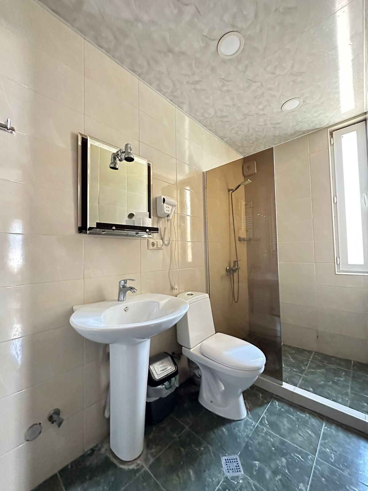 Un baño con lavamanos pedestal, inodoro, ducha y espejo.
