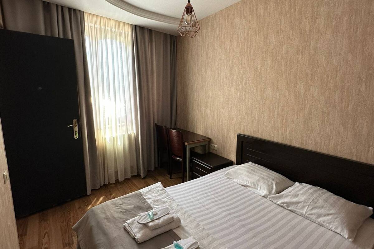 A hotel room with a large bed, a desk, a chair, and a wardrobe.