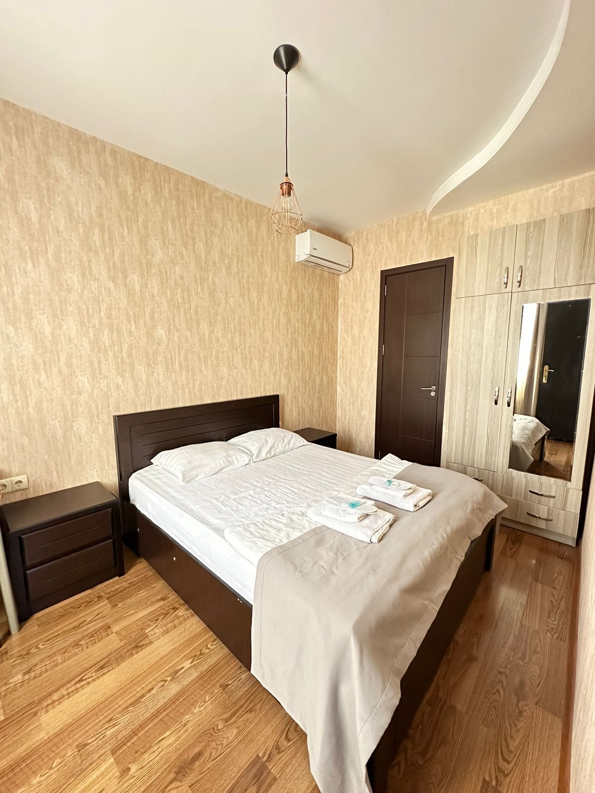A neatly arranged bedroom with a bed, bedside tables, a wardrobe, and an air conditioning unit.