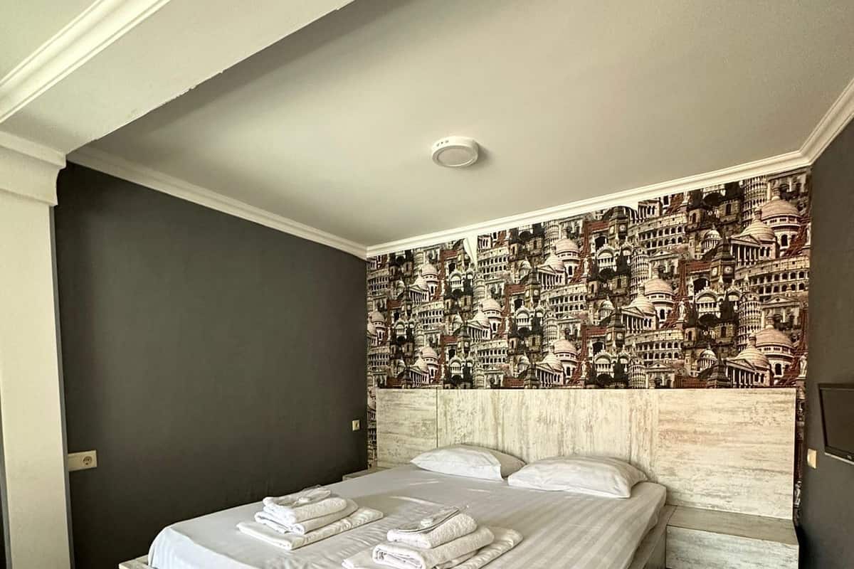 A bedroom with a large bed, a headboard with a cityscape wallpaper, and a wooden floor.