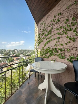 A balcony with a round table and chairs, a view of a cityscape, and a wall covered with ivy. - Hotel Piano (Tbilisi)
