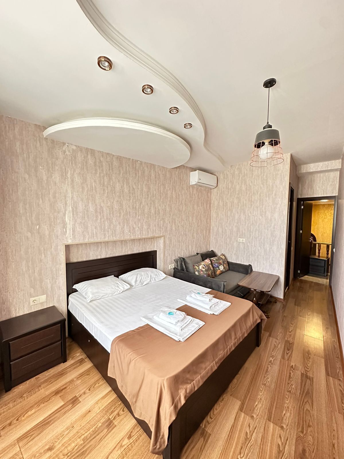 Una habitación de hotel moderna con una cama grande, un pequeño sofá, piso de madera y una lámpara en el techo.