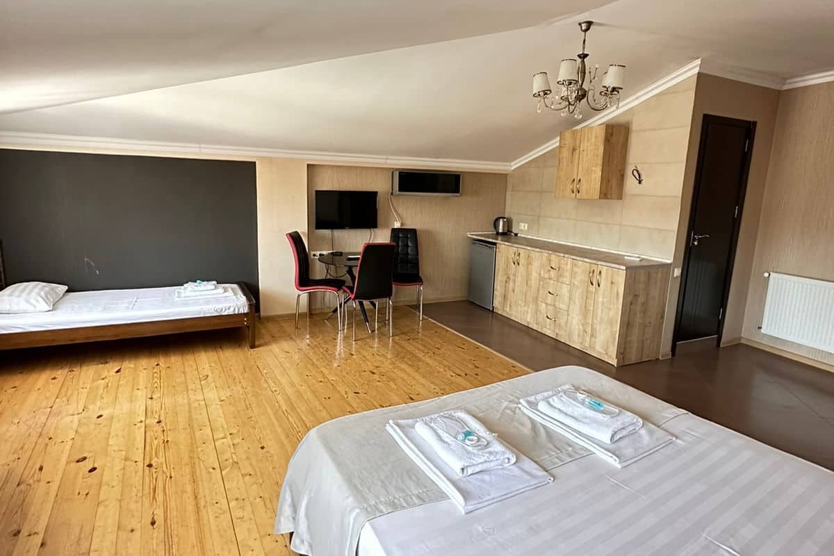 A modern hotel room with two beds, a kitchenette, a dining area, and a TV.