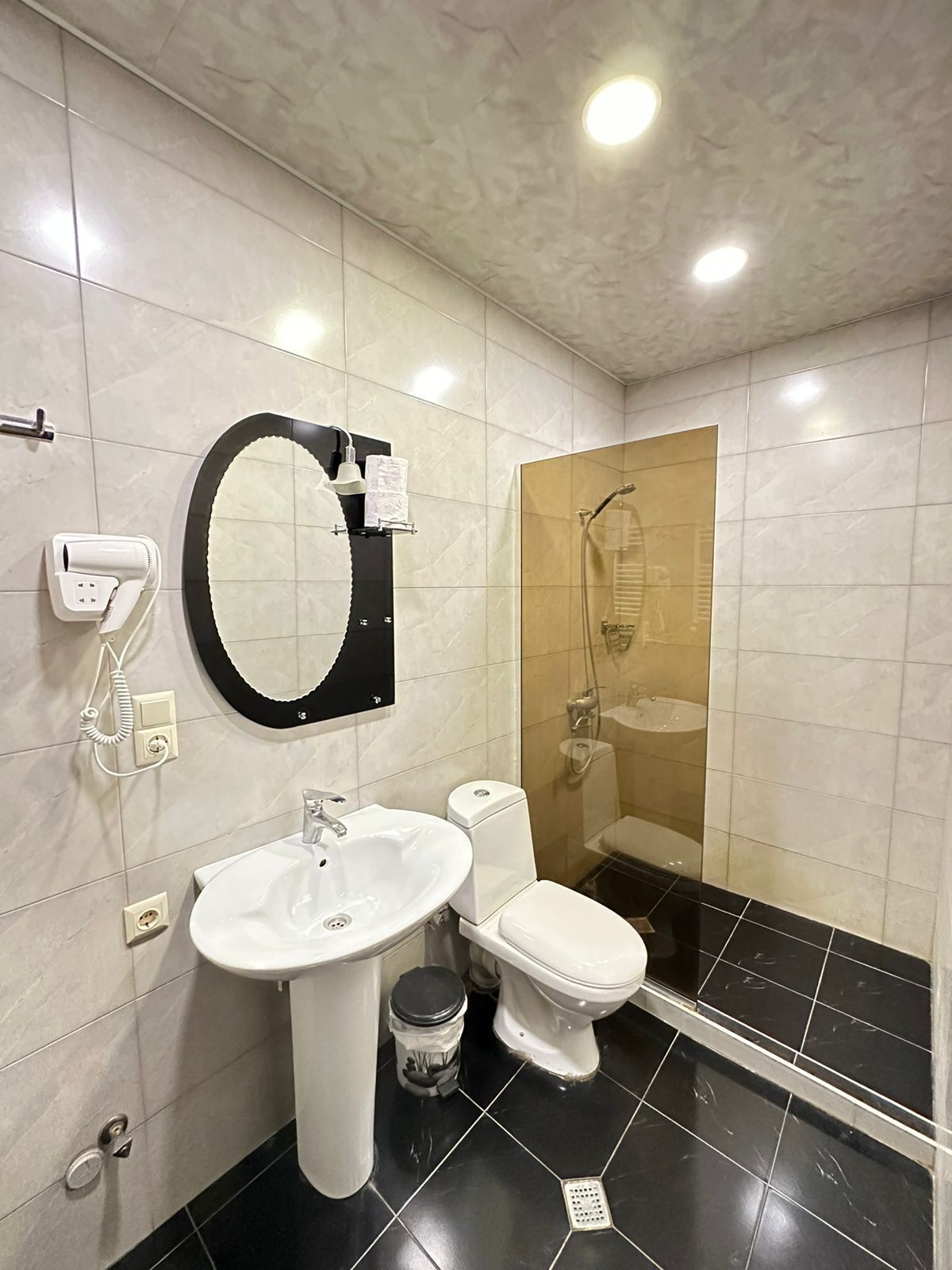 A modern bathroom with a white sink, toilet, and a glass-enclosed shower.