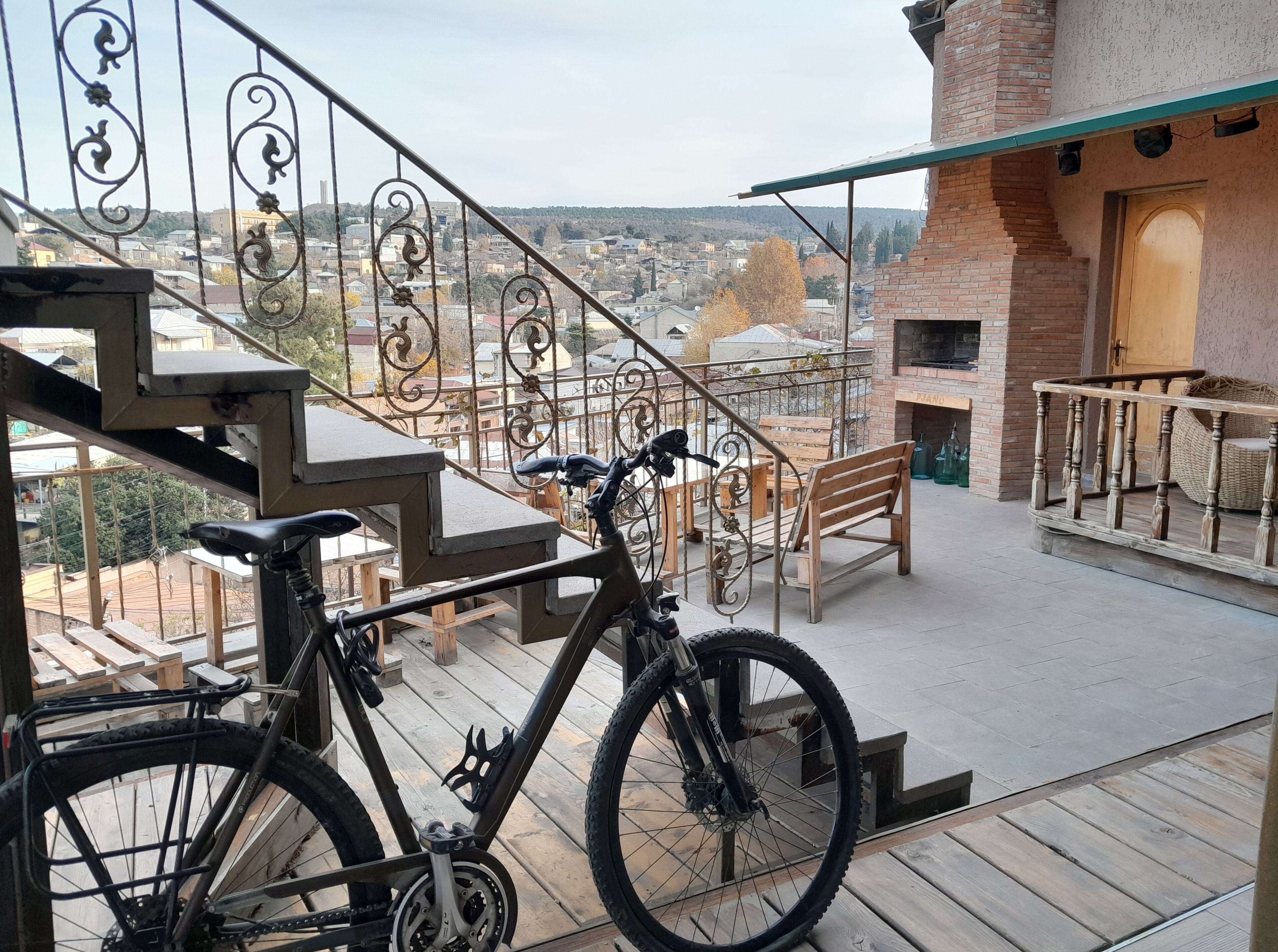 A balcony with a bicycle, wooden furniture, and a view of a cityscape.