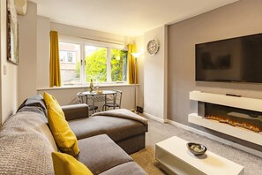 Een woonkamer met een bank, een televisie, een open haard en een eethoek met een tafel en stoelen.