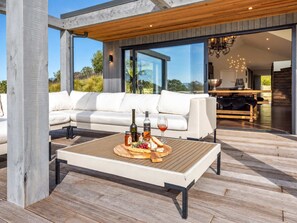 Ein moderner Außenbereich zum Sitzen mit einem Holztisch, einer weißen Couch und Blick auf den Küchen- und Essbereich.