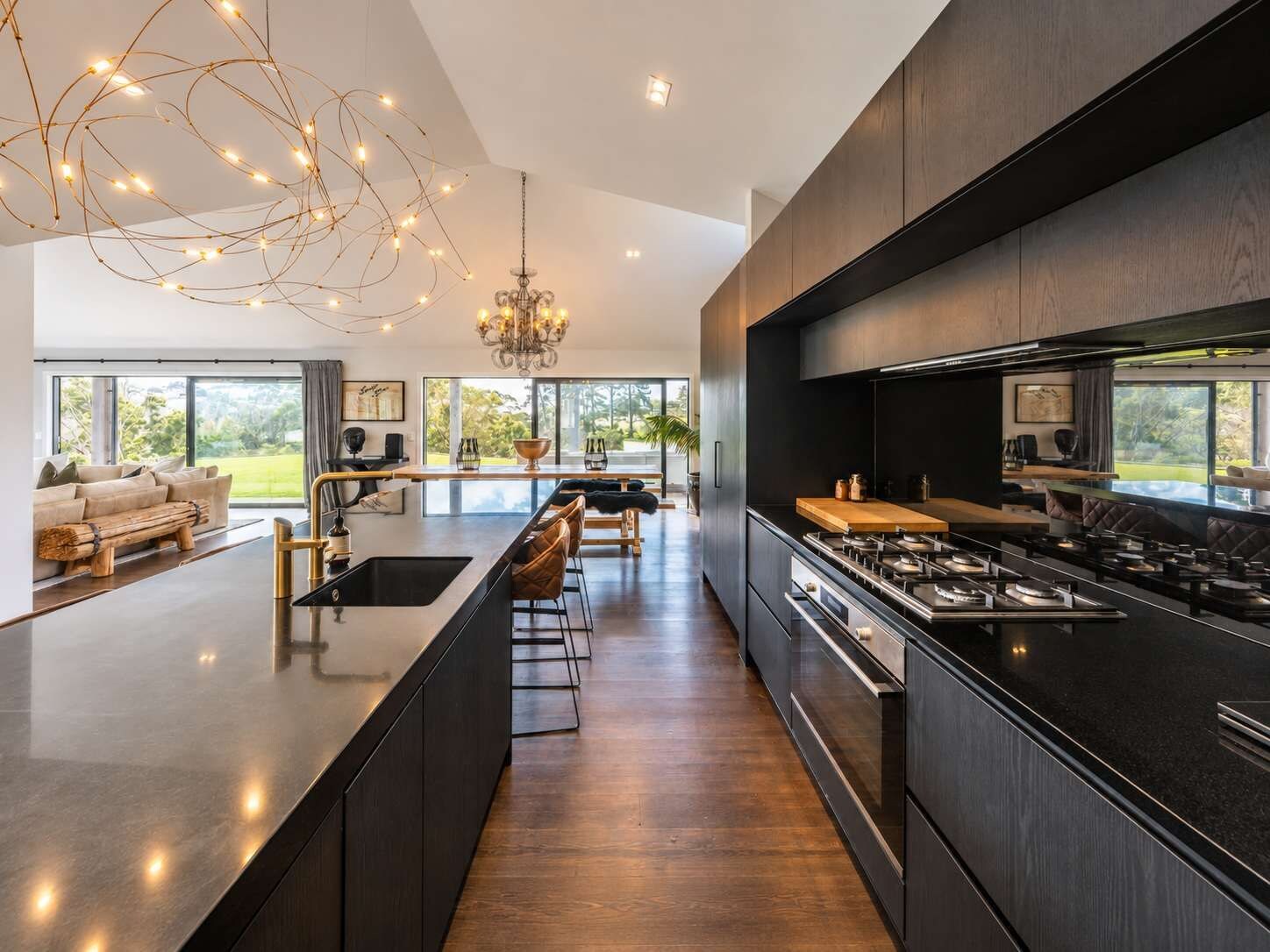 A modern kitchen with a central island, dark cabinetry, and a large window overlooking a garden.