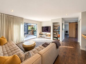 A modern living room with a sofa, a coffee table, and a television. There is a bookshelf and a sliding door leading to another room.