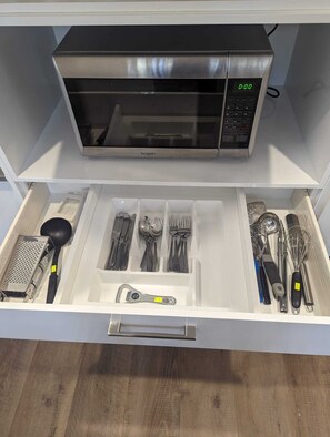 A kitchen drawer with utensils and a microwave.