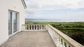 A balcony with a view of the sea and green fields.