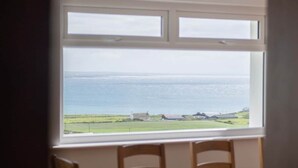A room with a large window offering a view of the sea and distant buildings.
