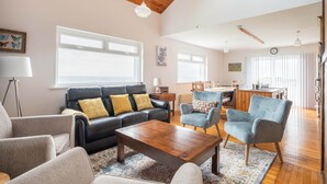A spacious living room with a wooden ceiling, a black leather sofa with yellow cushions, a wooden coffee table, and a blue armchair.