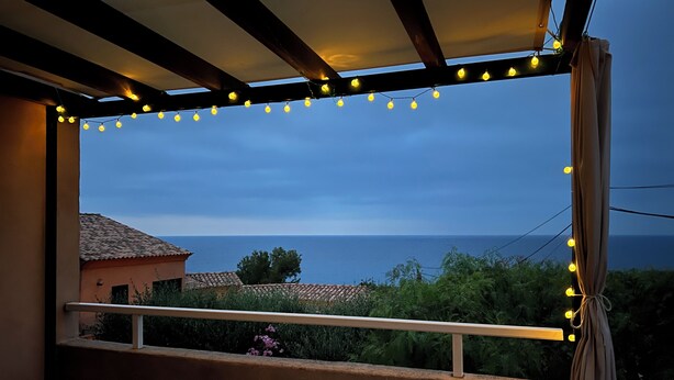 Un balcón con vistas al mar, luces cálidas y una mesa con sillas.