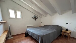 Un dormitorio con cama, un calefactor, una mesita pequeña y una lámpara de pared.