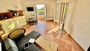 Un espacio habitable compacto con kitchenette, comedor y zona de estar con sofá y una mesita.