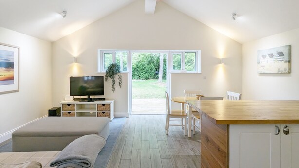 A spacious room with a high ceiling, a television, a dining area, and a view of the outdoors. - Millside, Bosham -  a bungalow that sleeps 4 guests  in 1 bedroom (Bosham)