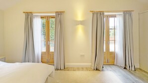 A bedroom with a large bed, two windows with curtains, a light fixture, and a wooden floor. - Millside, Bosham -  a bungalow that sleeps 4 guests  in 1 bedroom (Bosham)