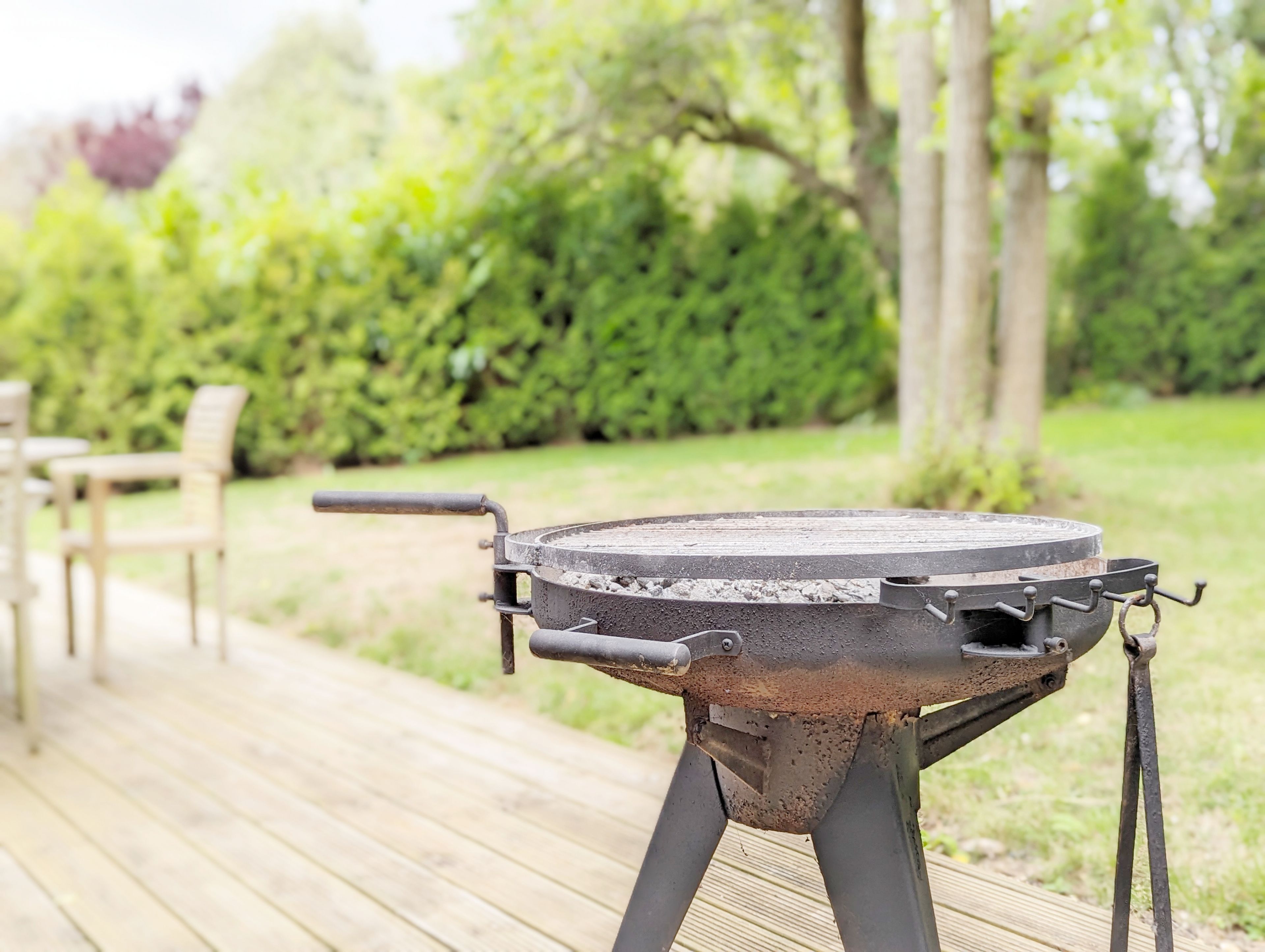 A barbecue grill on a wooden deck with a garden in the background.