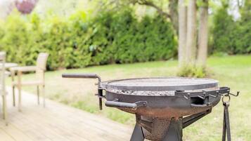 A barbecue grill on a wooden deck with a garden in the background.