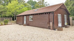 A wooden building with a sloped roof, a fenced area, and a gravel ground. - Millside, Bosham -  a bungalow that sleeps 4 guests  in 1 bedroom (Bosham)
