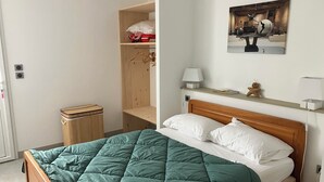 Ein ordentlich eingerichtetes Schlafzimmer mit einem hölzernen Bett, einer grünen Steude, einem Holzschrank, einem kleinen Nachttisch mit einer Lampe und einem an der Wand hängenden Kunstwerk.