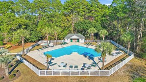 A swimming pool with lounge chairs, a small building, and a white fence.