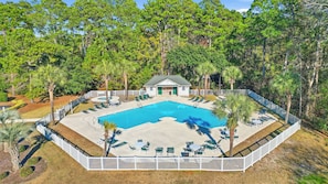 A swimming pool with lounge chairs, a small building, and a white fence.
