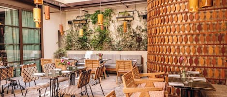 An outdoor seating area with tables and chairs, a wooden wall with a geometric pattern, and hanging pendant lights.