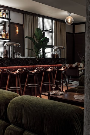 A bar area with stools, a bar counter, and a large plant. - Norman Hôtel & spa - Paris Champs-elysées (Paris)