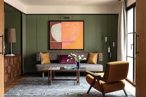 A modern living room with a sofa, a coffee table, and a chair. There is a painting on the wall and a lamp on the side.
