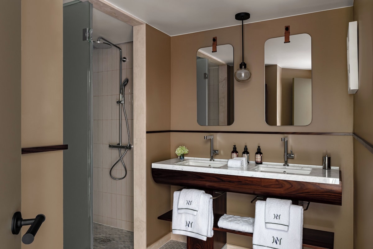 Un baño moderno con ducha, dos lavamanos y un espejo grande.