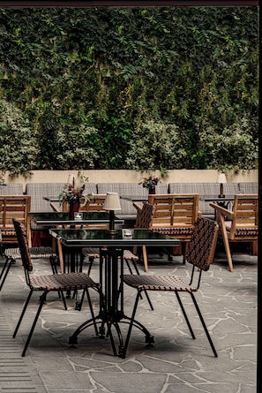 An outdoor seating area with a stone floor, wooden chairs, a table, and a wall covered in greenery.