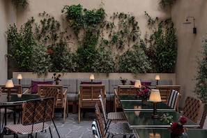 An outdoor seating area with tables and chairs, surrounded by lush greenery and a wall covered in plants. - Norman Hôtel & spa - Paris Champs-elysées (Paris)