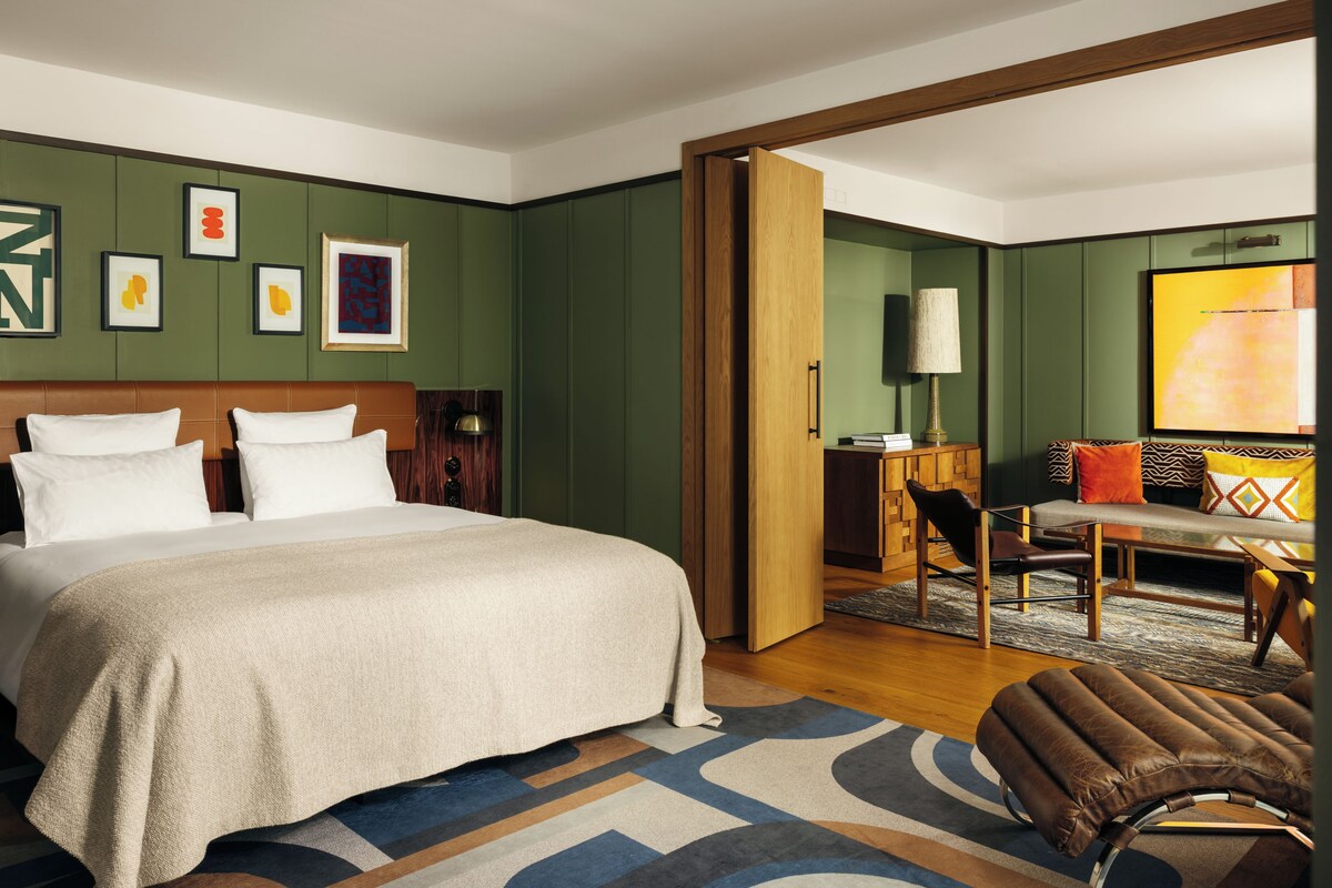 Una habitación de hotel con una cama grande, un escritorio, una silla y un sofá. Hay cuadros enmarcados en la pared y un televisor también allí.