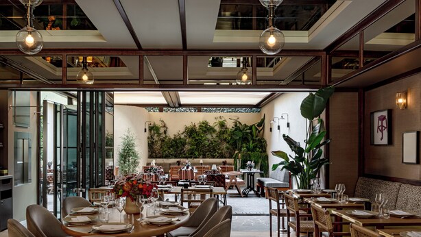 A restaurant with a modern interior, featuring wooden tables and chairs, a large potted plant, and a view of the outdoor seating area. - Norman Hôtel & spa - Paris Champs-elysées (Paris)