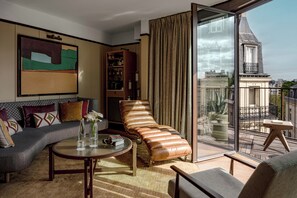 A modern living room with a sofa, a chaise lounge, a round coffee table, and a glass door leading to a balcony.