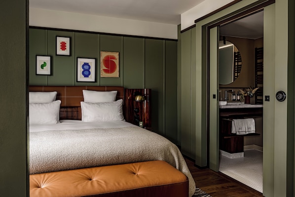 Une chambre à coucher bien rangée, avec un lit, un banc et une salle de bain visible à travers une porte ouverte.