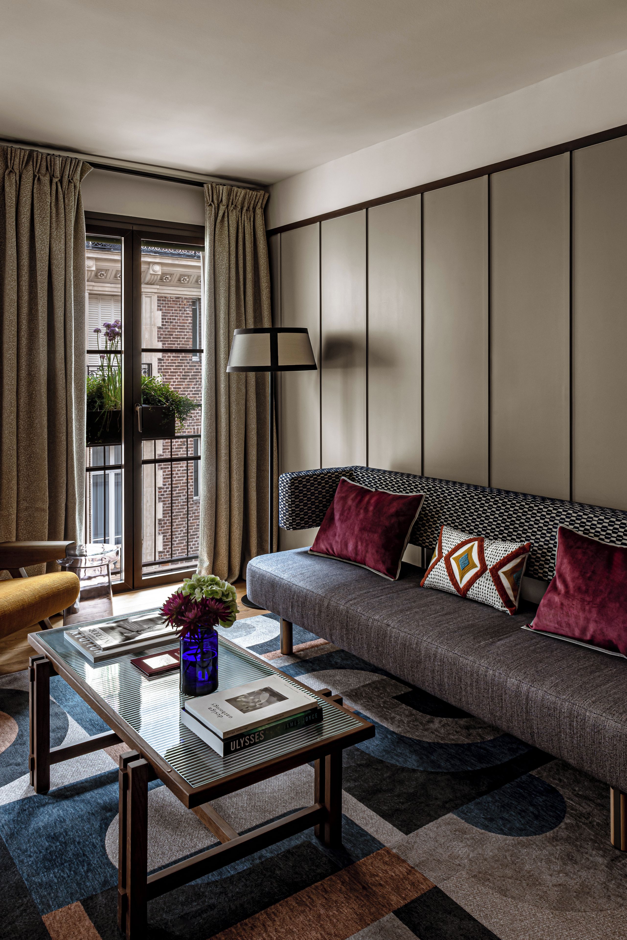 A modern living room with a sofa, a glass coffee table, a lamp, and a view of the outside.