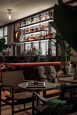 A bar area with shelves of bottles, a bar counter, and seating with tables and chairs. - Norman Hôtel & spa - Paris Champs-elysées (Paris)